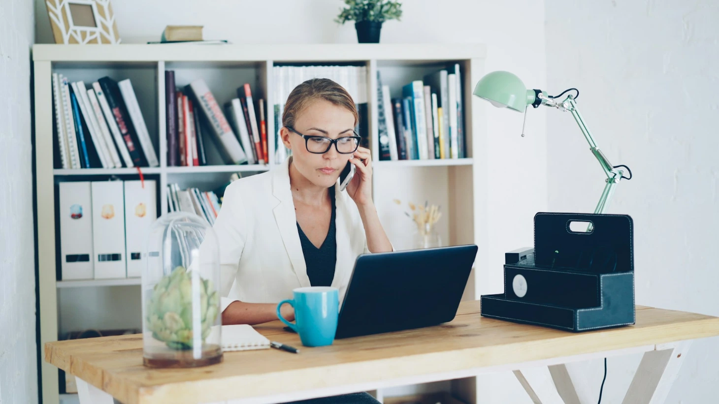 Woman on phone at desk with laptop and books