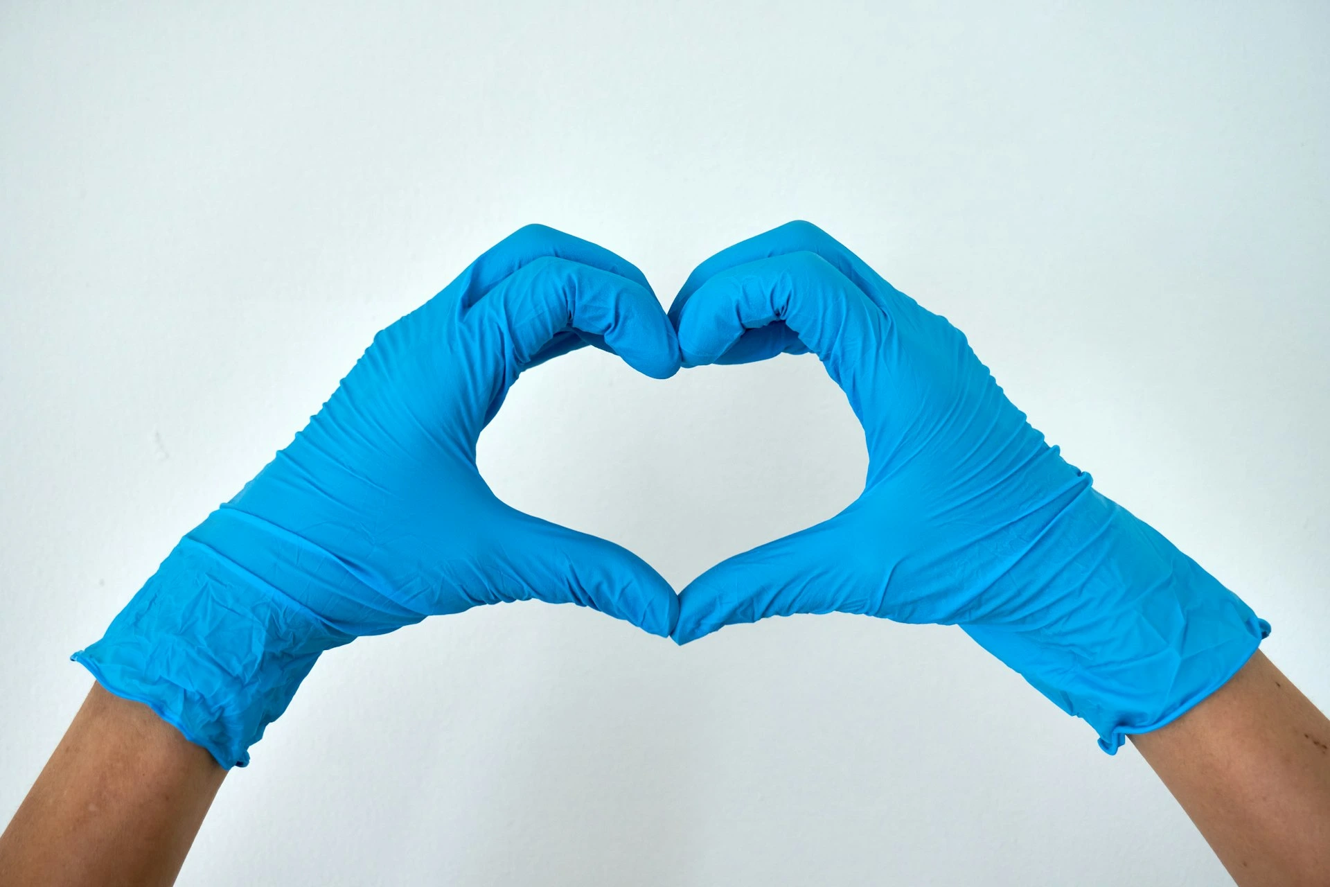Hands in blue nitrile gloves forming a heart shape against a white background